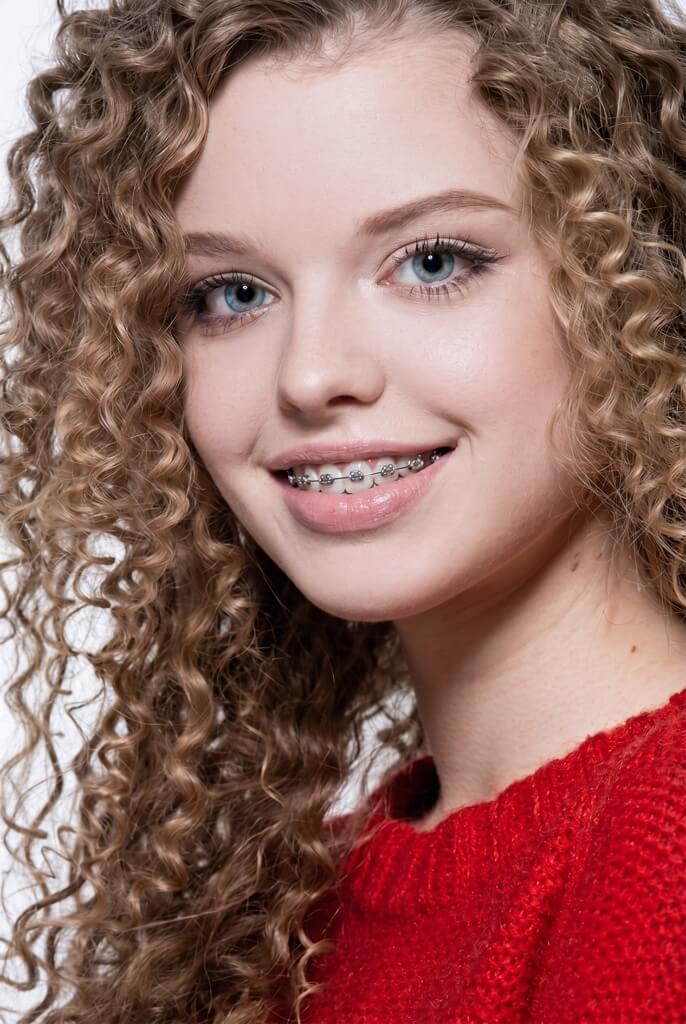 Teenage girl with curly hair and fixed braces smiling at the camera