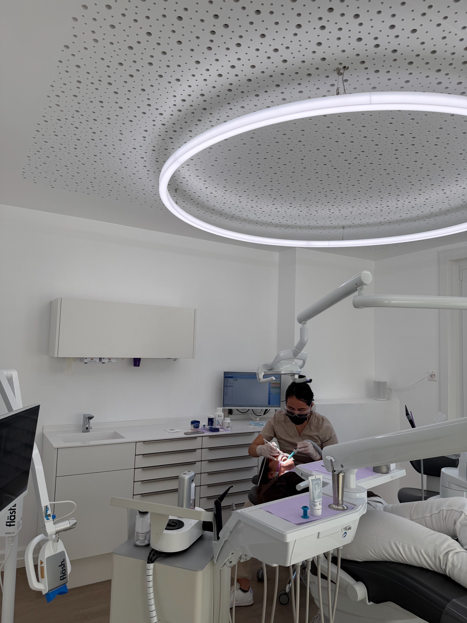 Behandlung einer Patientin im Behandlungszimmer der Zahnarztpraxis Karamousli unter runder Ringleuchte