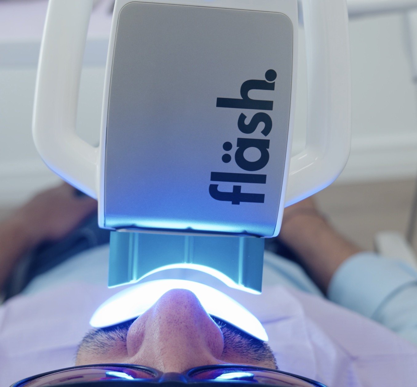 Patient mit Schutzbrille unter der blau leuchtenden fläsh-Bleaching-Lampe in der Zahnarztpraxis Karamousli