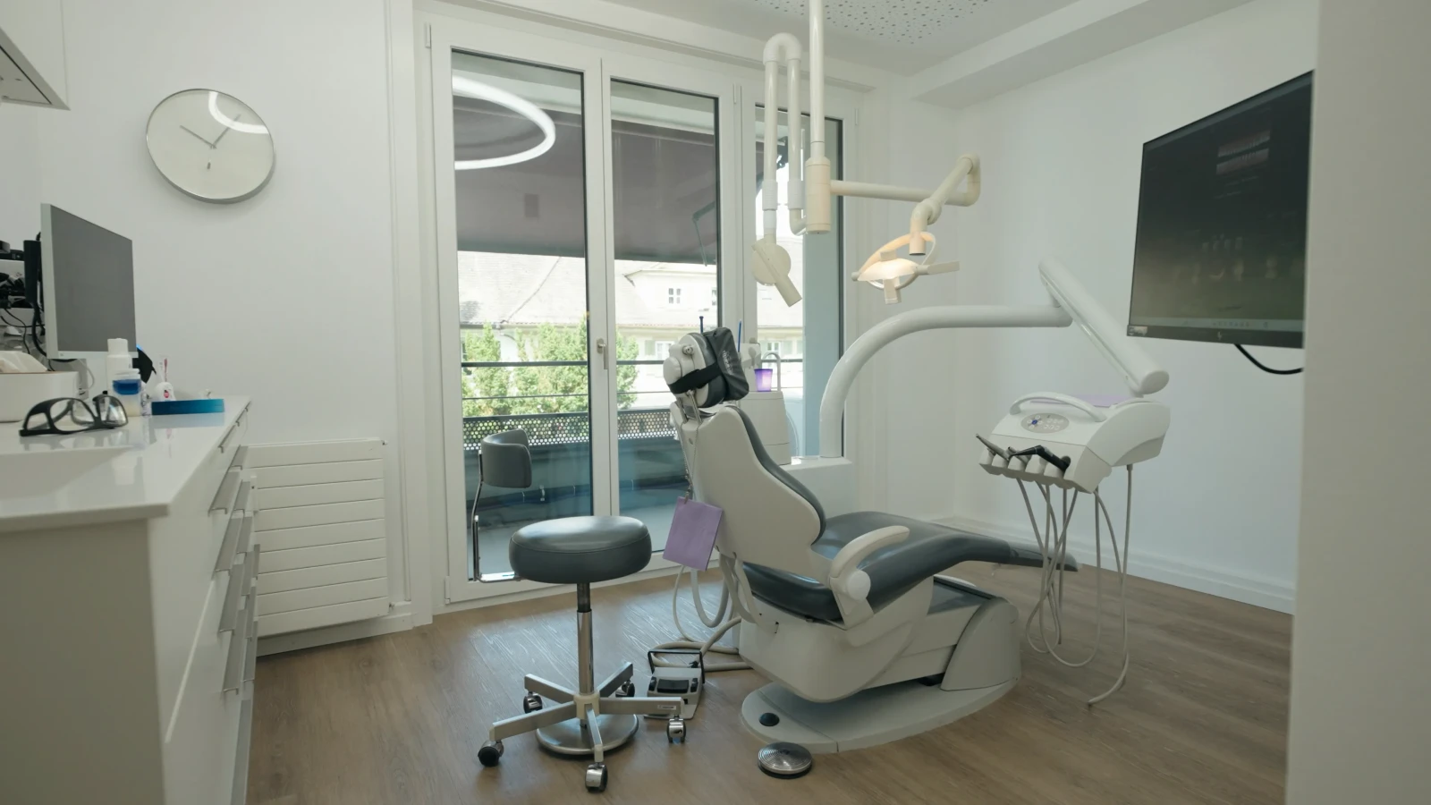 Behandlungszimmer mit Behandlungsstuhl, Wandbildschirm und Balkontür