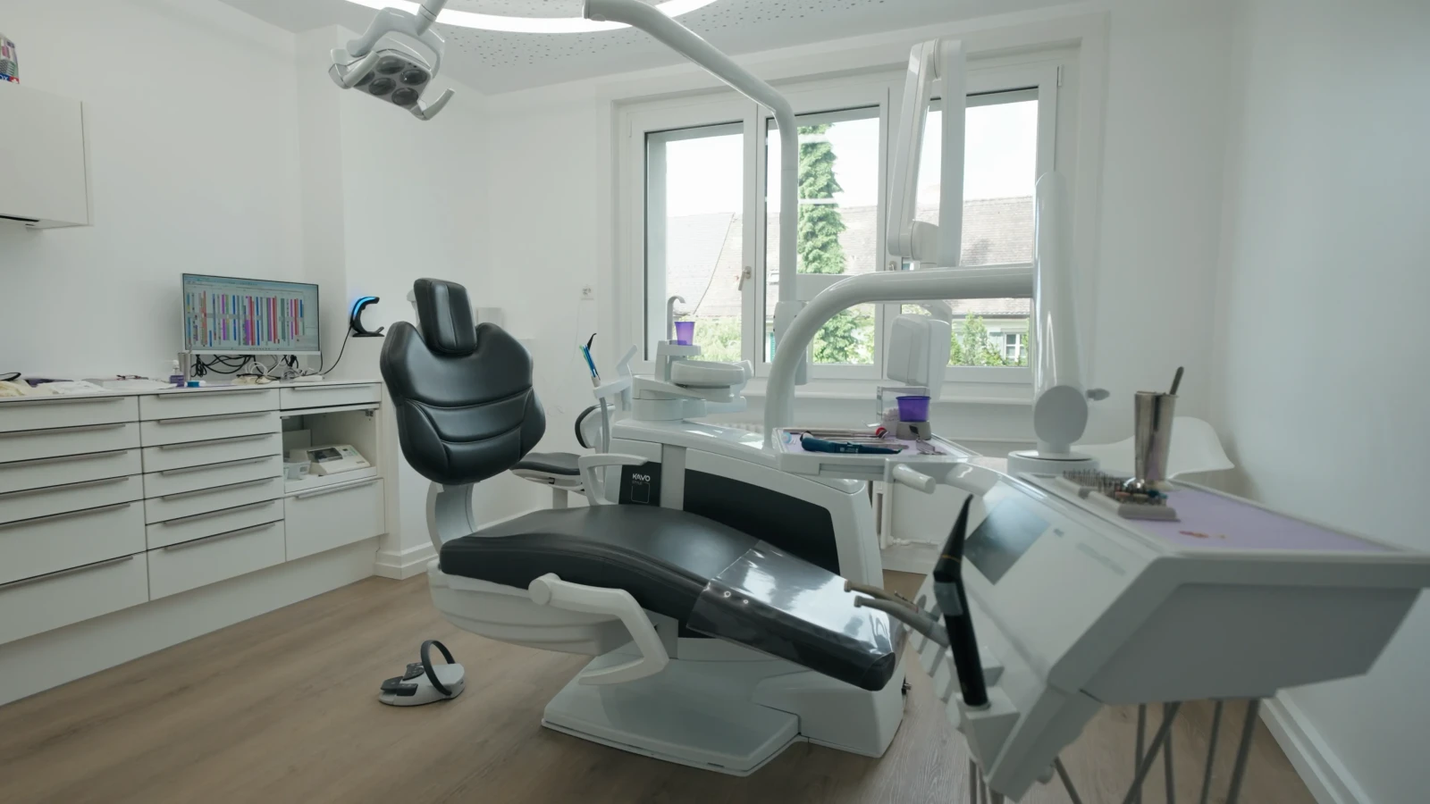 Behandlungszimmer mit Behandlungsstuhl, Schrankzeile und Fenstern in der Zahnarztpraxis Karamousli