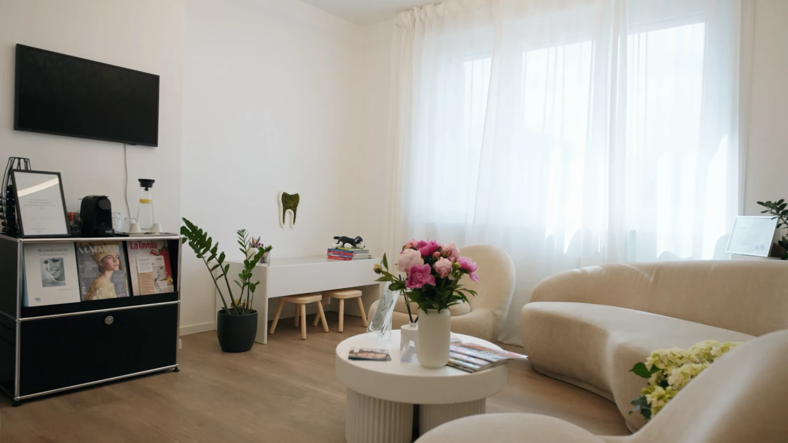 Wartebereich mit Sofa, Zeitschriften und Kinderecke in der Zahnarztpraxis Karamousli