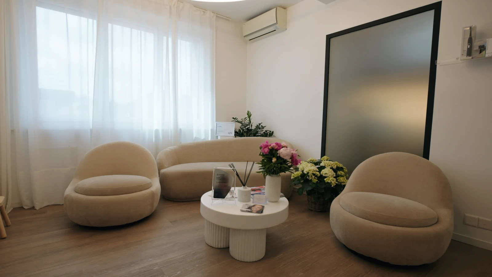 Heller Wartebereich der Zahnarztpraxis Karamousli in Küsnacht mit runden Sesseln, Sofa und Blumen